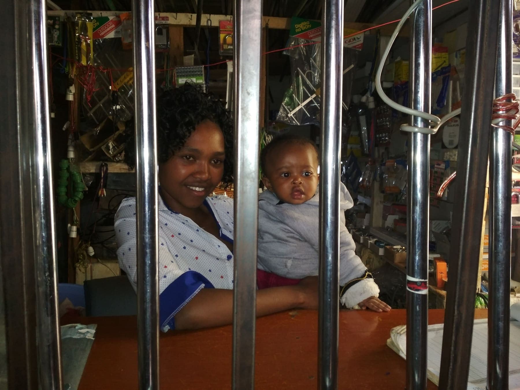 A shopkeeper holding her baby behind the counter of a Kenyan electricals and hardware shop